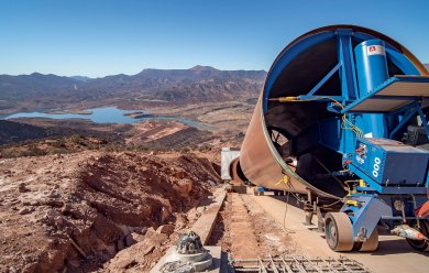 Un mélangeur de ciment industriel sur un chantier avec en arrière-plan un lac et des montagnes sous un ciel bleu