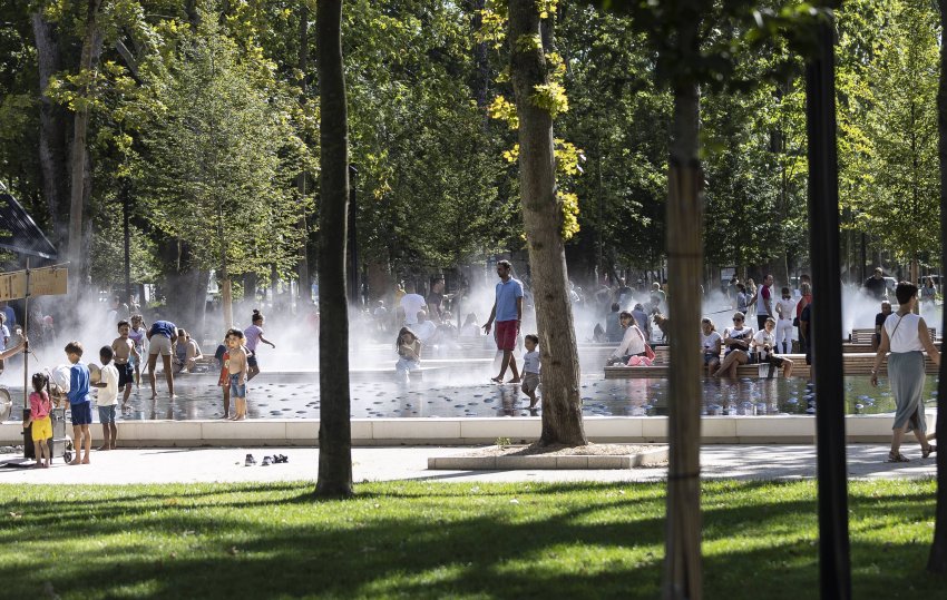 Des familles et des enfants profitent d’une fontaine d’eau dans un parc ensoleillé.