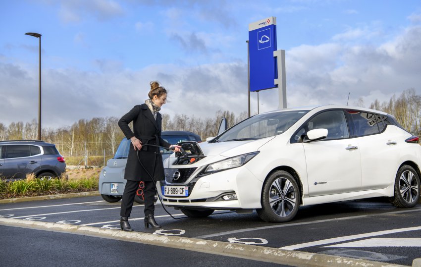 Une personne se prépare à charger une Nissan Leaf électrique blanche dans un parking réservé aux véhicules électriques.