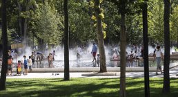 Des familles et des enfants profitent d’une fontaine d’eau dans un parc ensoleillé.