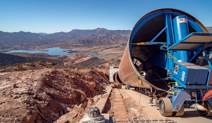 Un mélangeur de ciment industriel sur un chantier avec en arrière-plan un lac et des montagnes sous un ciel bleu
