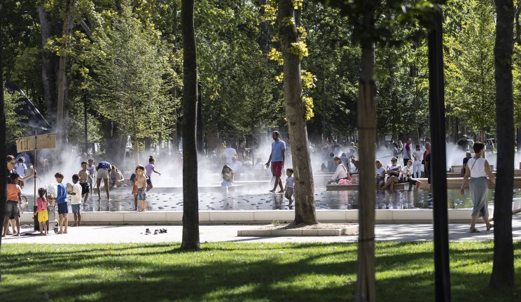 Des familles et des enfants profitent d’une fontaine d’eau dans un parc ensoleillé.