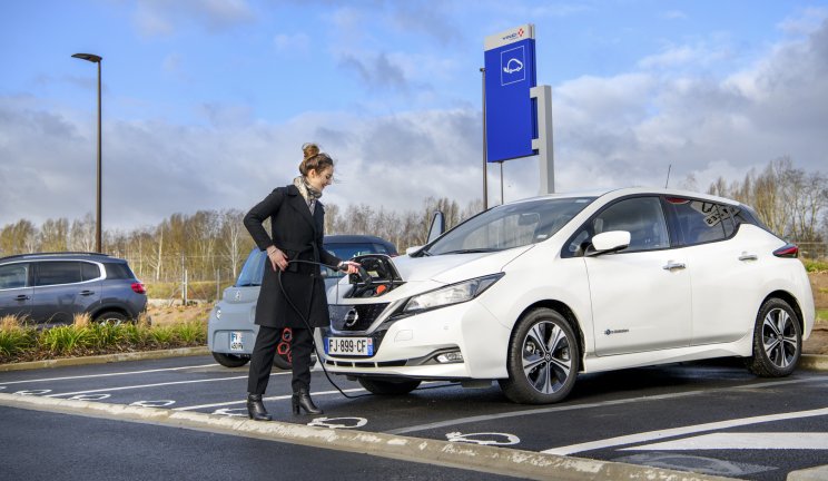 Une personne se prépare à charger une Nissan Leaf électrique blanche dans un parking réservé aux véhicules électriques.